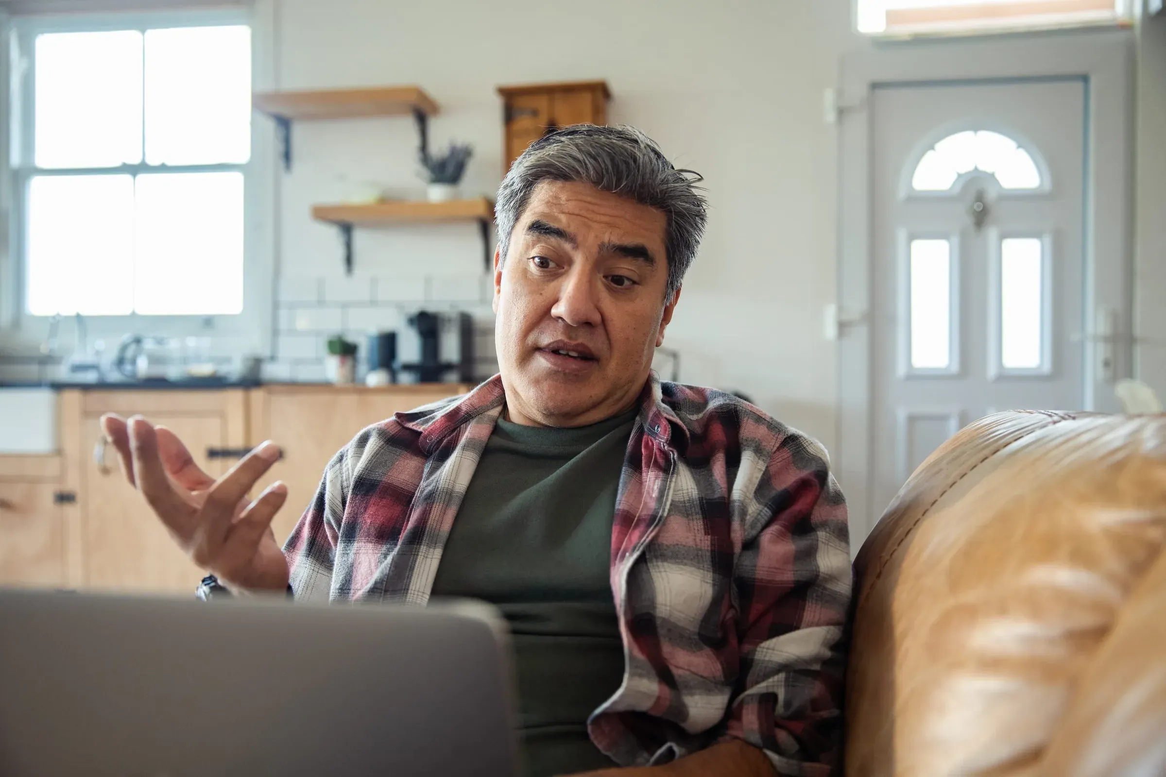 A man on a sofa with a laptop, mid-conversation gesture