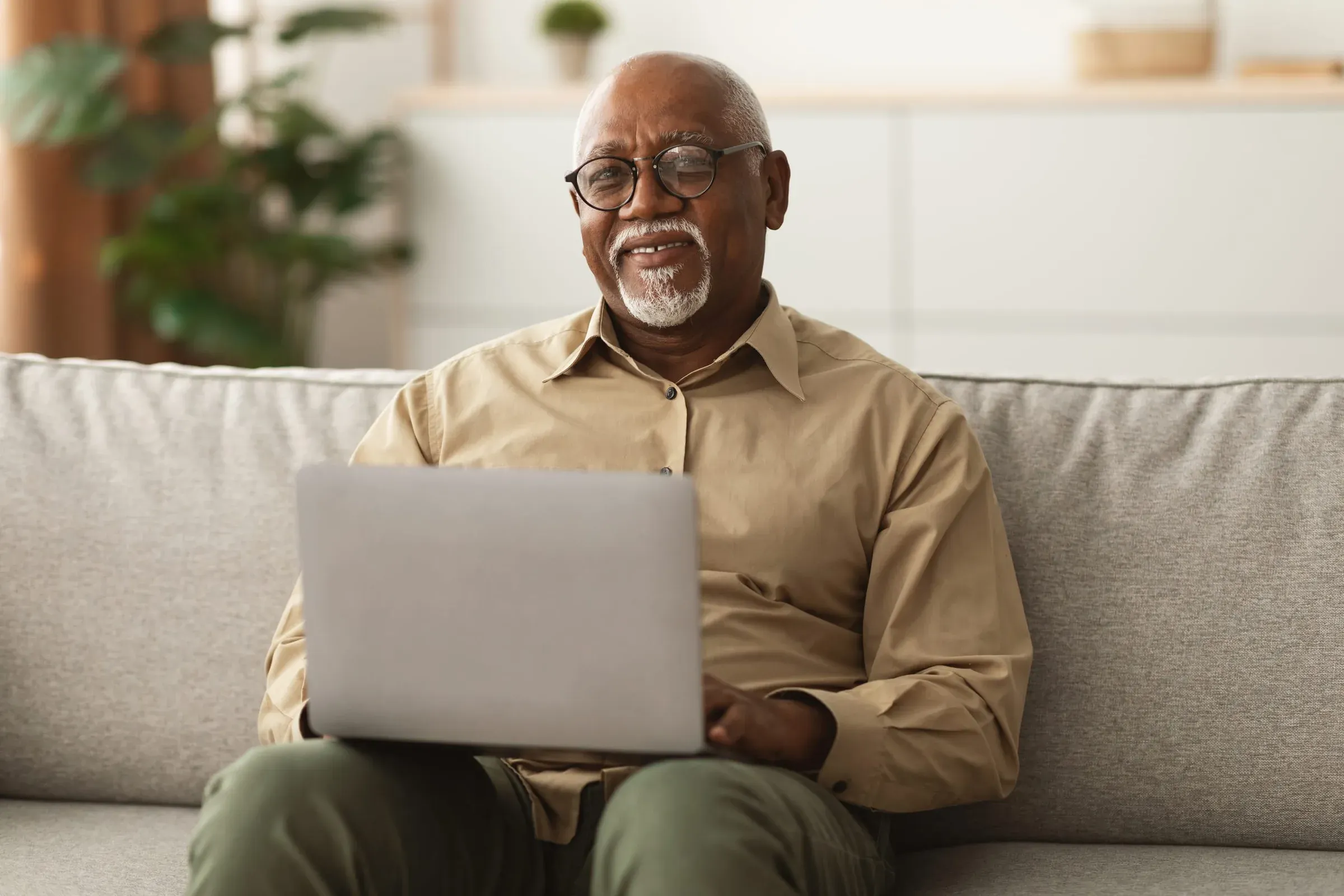 An older man on a sofa contentedly using a laptop