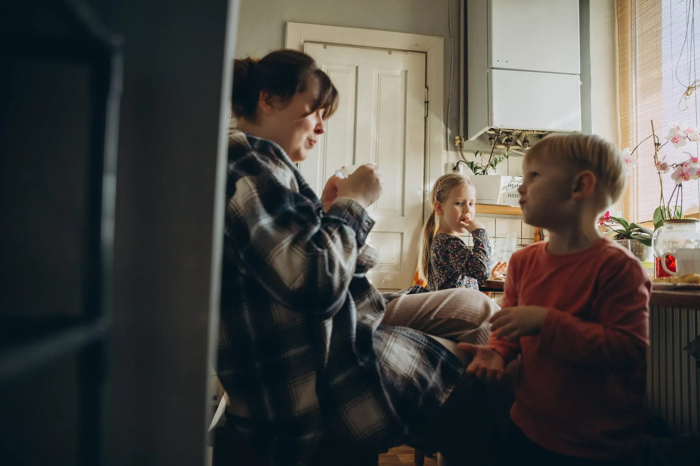 A mother with two young children in a lived-in kitchen, soft window light
