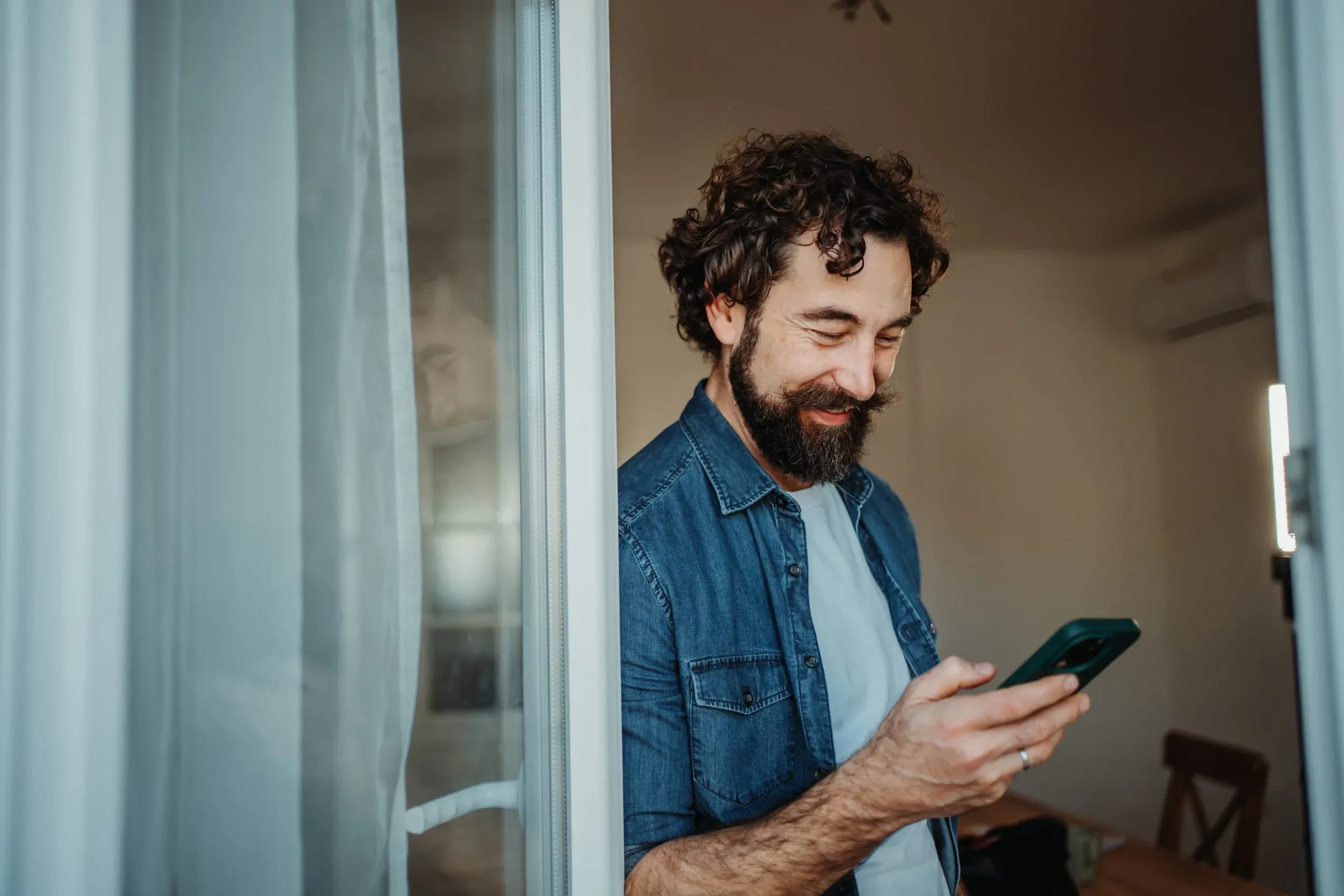 A man at home looking at his phone, smiling