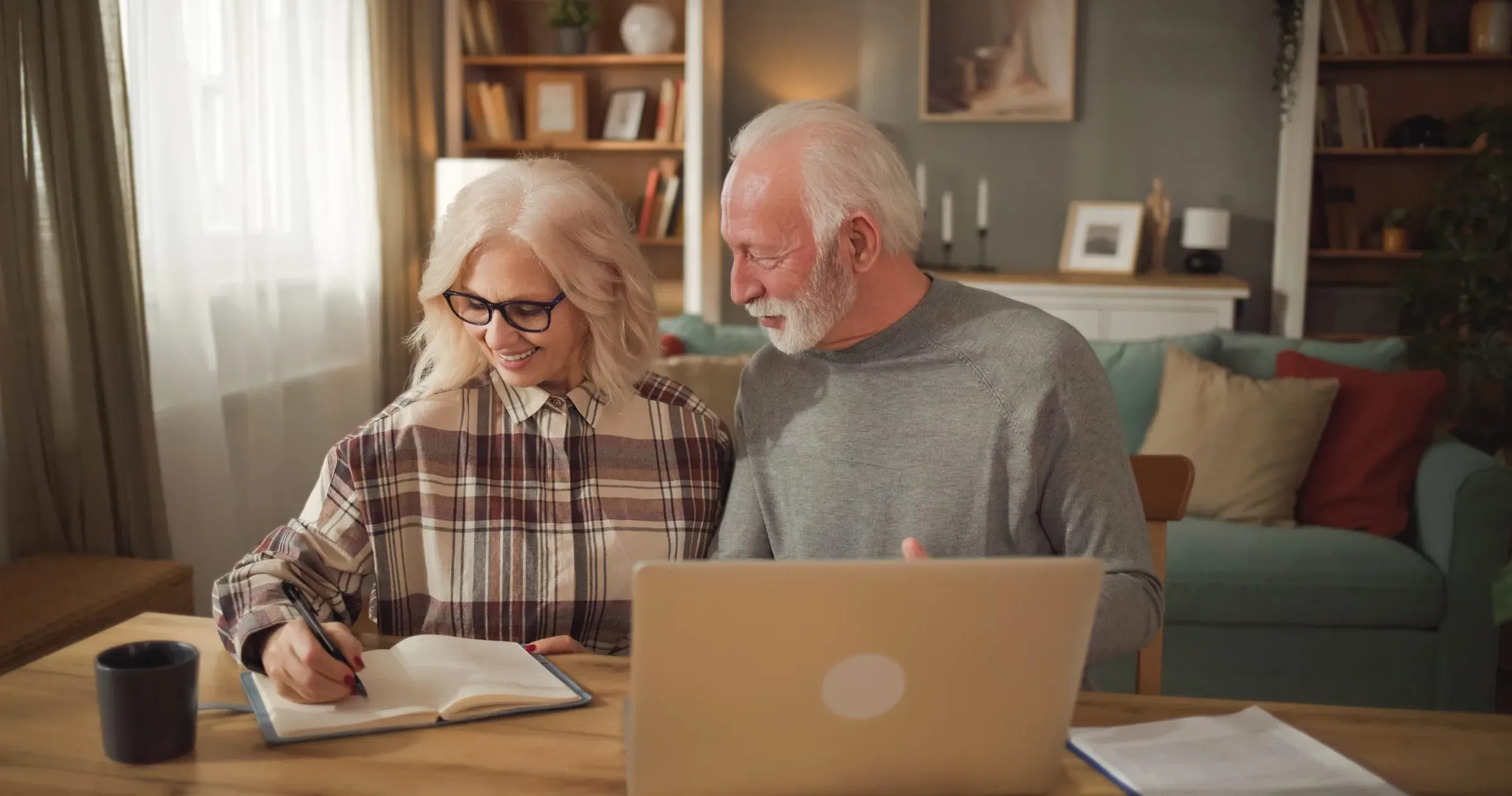 An older couple at a kitchen table working through their plans together with a notebook and laptop