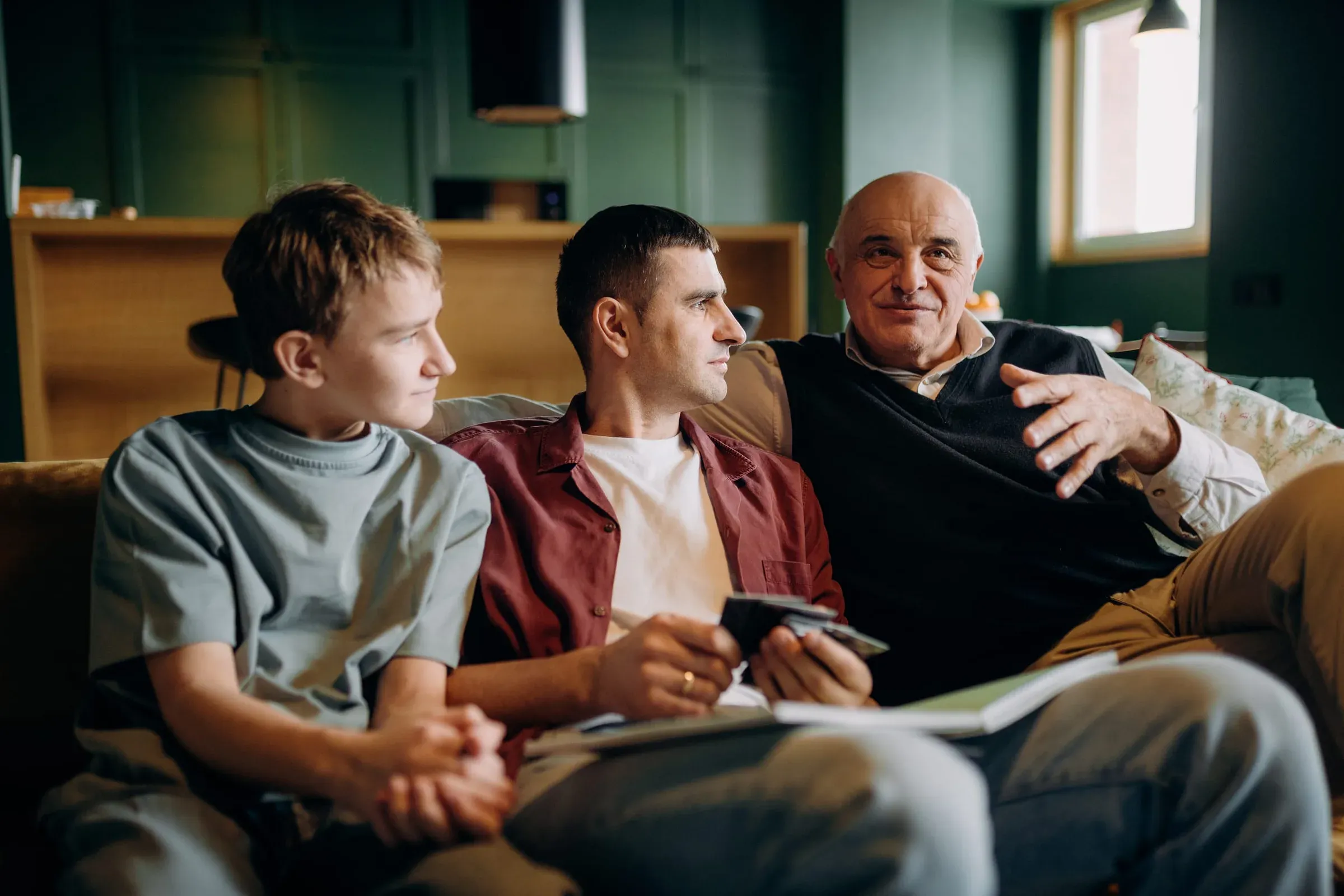 Three generations of men on a sofa, mid-conversation, with a notebook on their lap