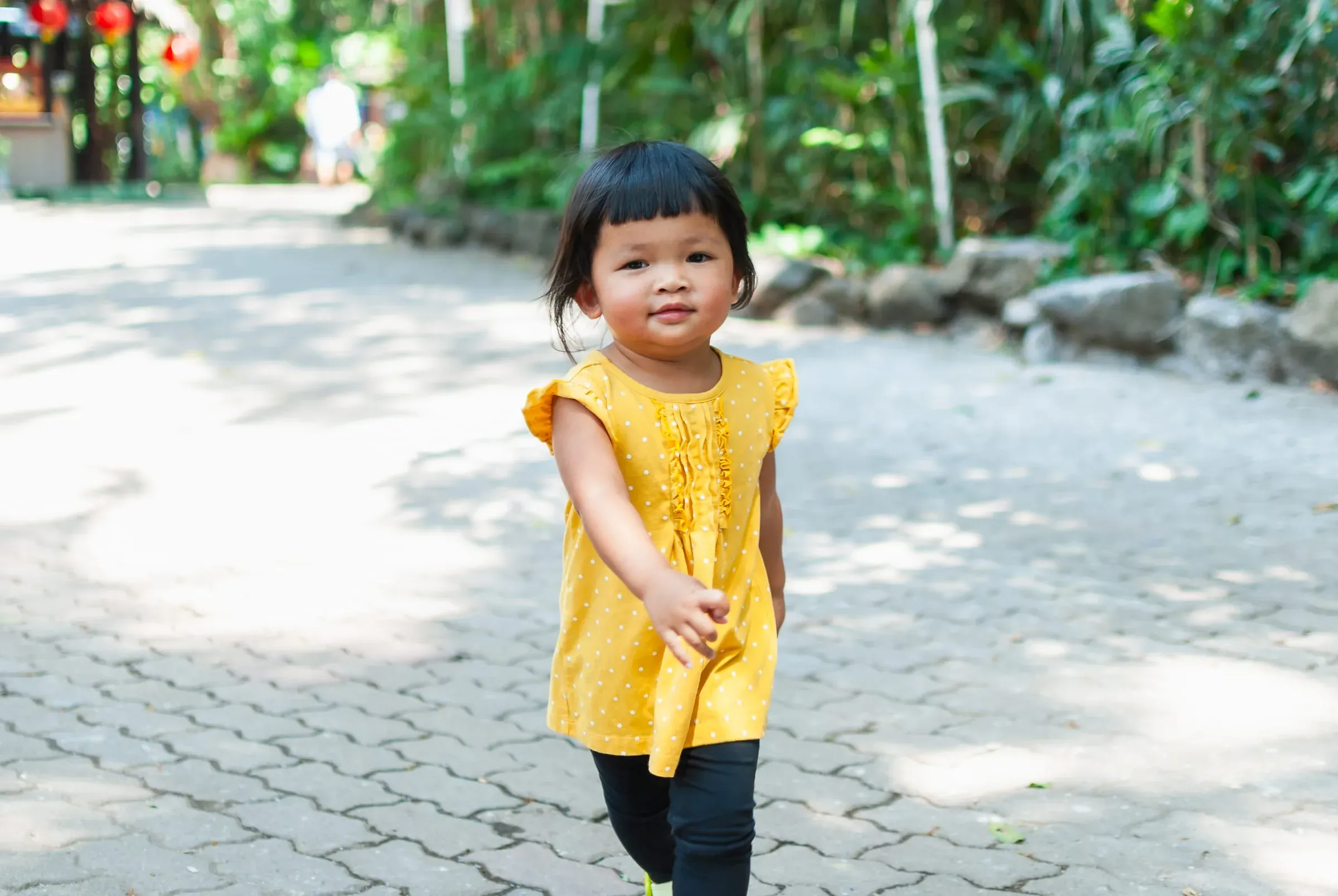 A young child in a yellow dress walking along a brick path