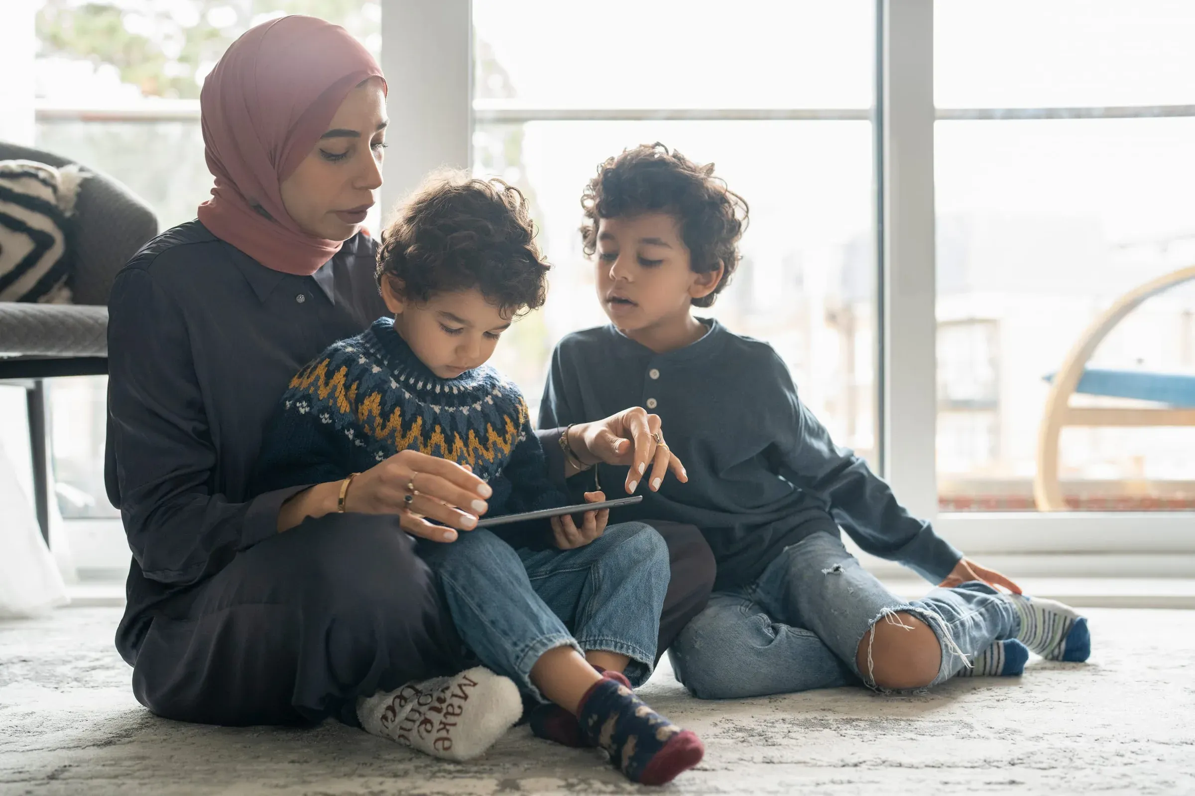 A mother and her two children sitting on the floor reading from a tablet